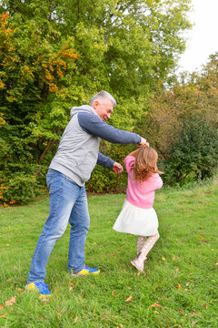 Grandfather and little girl dancing together in autumn park