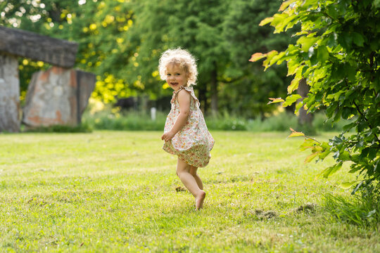 Smiling toddler running barefoot on sunny park lawn