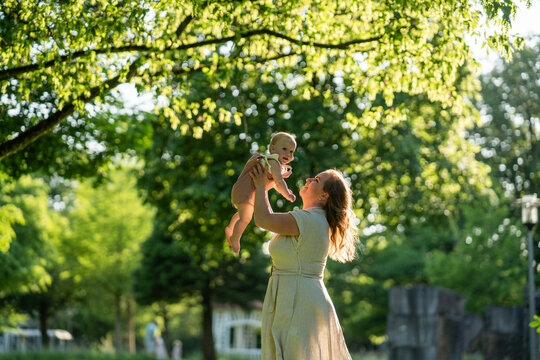 Mother lifting baby girl in sunny park during summer