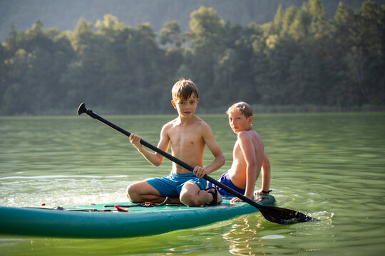 Children paddleboarding on calm lake during summer vacation