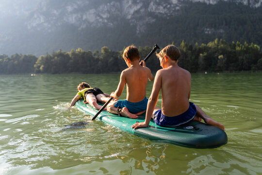 Children playing on paddleboard at lake in summer vacation