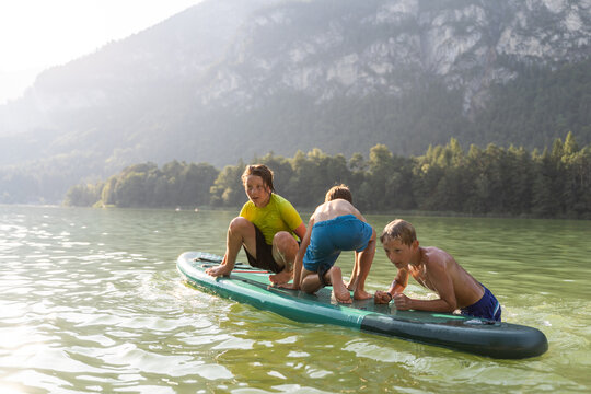 Children play on paddleboard at mountain lake in summer