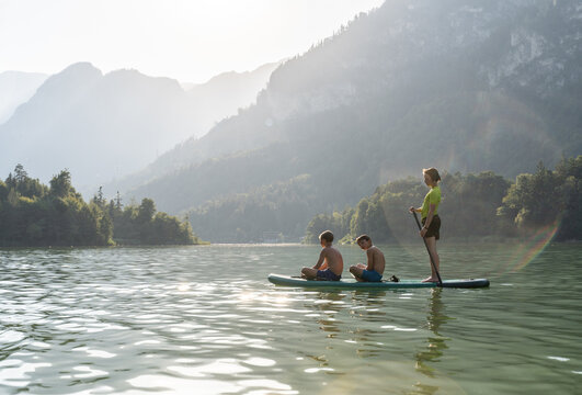 Children paddleboarding on mountain lake in summer vacation