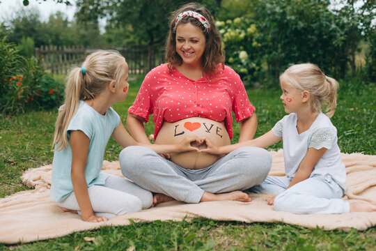 Pregnant mother with daughters making heart on belly outside