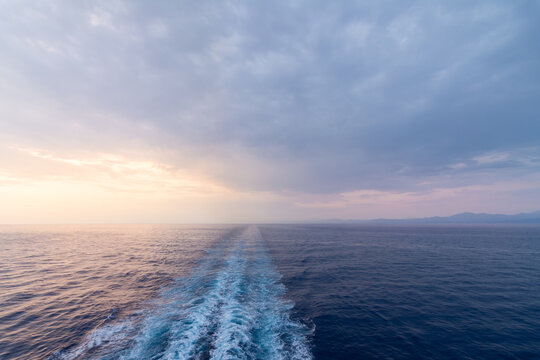 Serene ocean sunset with ship wake and distant coast