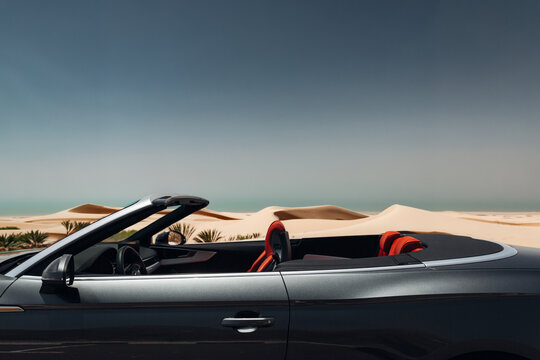 Luxury convertible car parked by desert dunes at sunset
