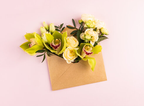 Floral bouquet in kraft envelope on pastel pink background