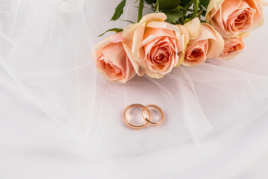 Wedding rings with rose bouquet on bridal veil background