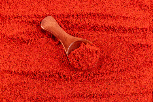 Close-up of red ground spice with wooden scoop texture