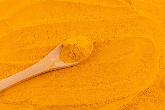 Turmeric powder with wooden spoon on spice background