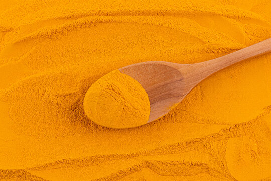 Turmeric powder with wooden spoon on spice background