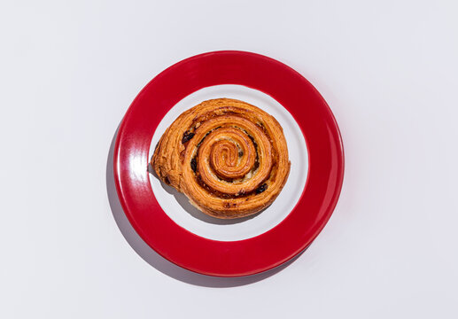 Spiral raisin pastry on red plate, bakery treat