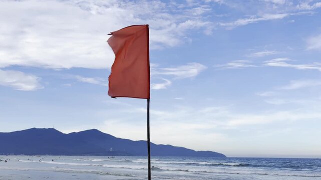 Video of a red warning flag on a beach by the sea, indicating dangerous swimming conditions and restricted access to water. Coastal safety concept with ocean waves and seaside atmosphere.