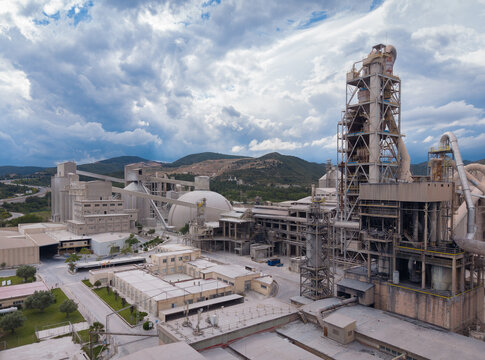 Elevated view of a large cement manufacturing facility featuring a multi-stage cyclone preheater tower, spherical clinker storage dome, vertical silos, rotary kiln structure and conveyor systems