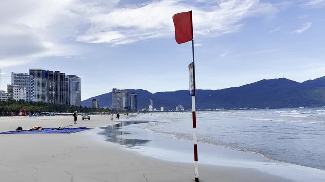 Video of a red warning flag on a beach by the sea, indicating dangerous swimming conditions and restricted access to water. Coastal safety concept with ocean waves and seaside atmosphere.