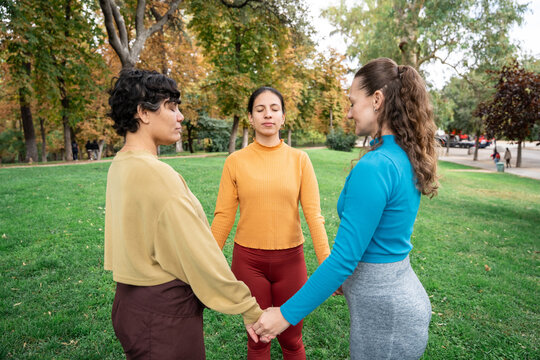 Three women holding hands in park meditation retreat circle