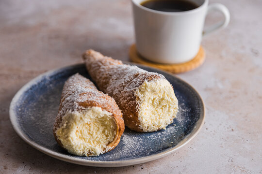 Conic cannoli coated with sugar on plate with coffee