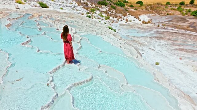 Woman traveler at Travertines of Pamukkale, Turkey. Female visitor walks through turquoise thermal pools on white limestone terraces.