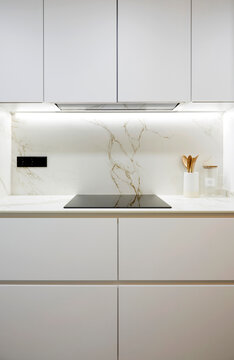 Modern white kitchen with marble backsplash and cooktop