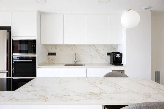 Minimal white kitchen with marble surfaces and built in oven