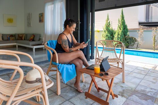 Woman working by pool with smartphone and tablet outdoors