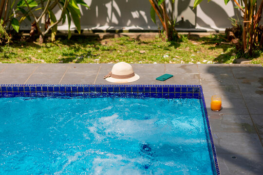 Summer poolside scene with sunhat, phone, and drink