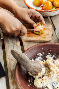 Preparing sambal with hands slicing tomato on cutting board