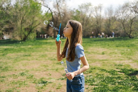 Girl blowing soap bubbles in sunny spring park outdoors