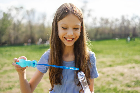 Smiling girl blowing soap bubble outdoors in spring park