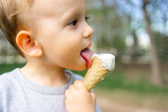Toddler licking vanilla ice cream cone outdoors in summer
