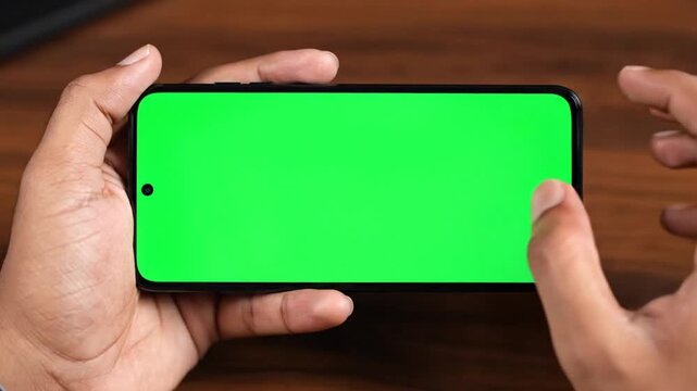 Person holding a smartphone with a green screen interface and performing swiping gestures to interact with the digital display during a professional tech product presentation