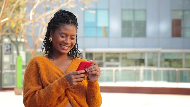 Joyful young woman happily engaged with her smartphone, showcasing a bright smile while enjoying her day outdoors, embodying a moment of connection, excitement, and modern technology.