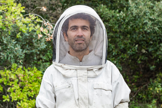 Beekeeper in protective gear with lush green background