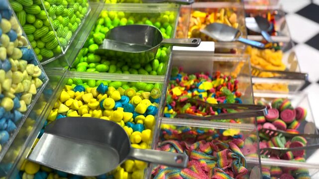 Vibrant display of assorted candies and gummy sweets in clear plastic dispensing bins with metal scoops at a confectionery shop, offering a wide choice of sugary treats for customers