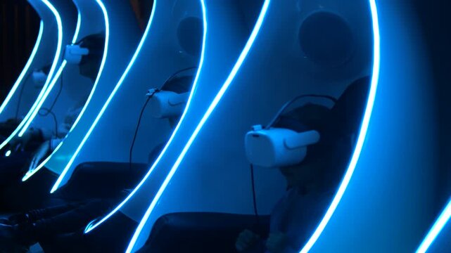 Row of people sitting in futuristic chairs with glowing blue neon lights, wearing vr headsets and experiencing immersive augmented reality entertainment in a dark room at an amusement park