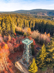 Fototapeta premium Slovanka Lookout Tower stands tall in the Jizera Mountains, showcasing vibrant autumn colors. This historic iron tower offers stunning views of the surrounding forested landscape.