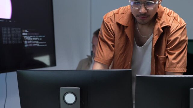 A focused software engineer wearing glasses and gesturing while presenting machine learning workflows and database scripts on multiple office screens.