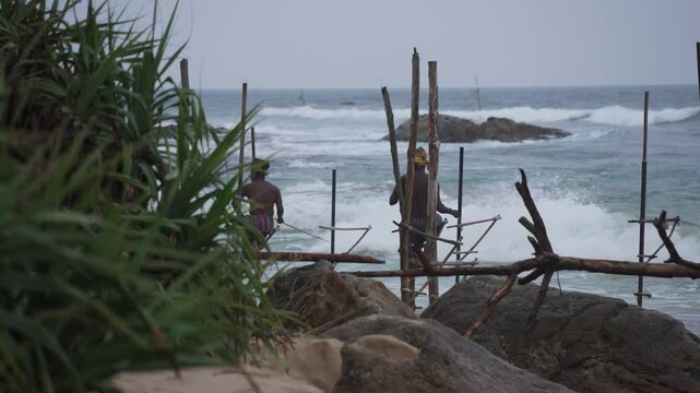 View of waves and beach with local fishermen demonstrating on-water stilt fishing, Koggala, Sri Lanka, Asia