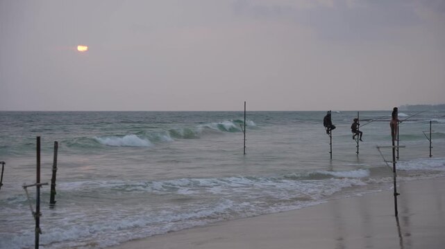 View of waves and beach with local fishermen demonstrating on-water stilt fishing, Koggala, Sri Lanka, Asia