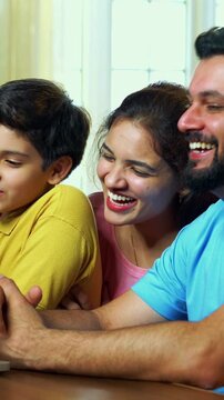 Family watching comedy on laptop together and laughing joyfully while bonding at dining table
