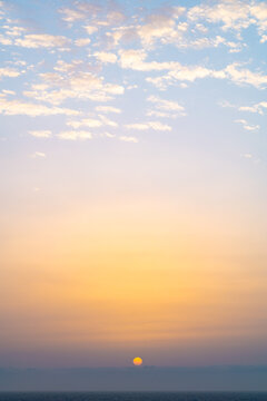 Pastel sunrise over calm ocean with soft cloud sky
