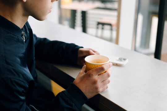 Teenage boy holding warm drink at cafe counter by window