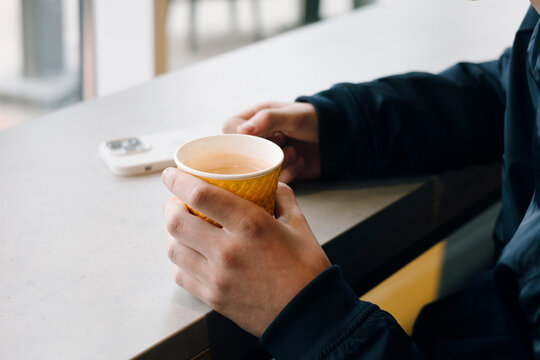 Person holding hot coffee cup at cafe table near phone
