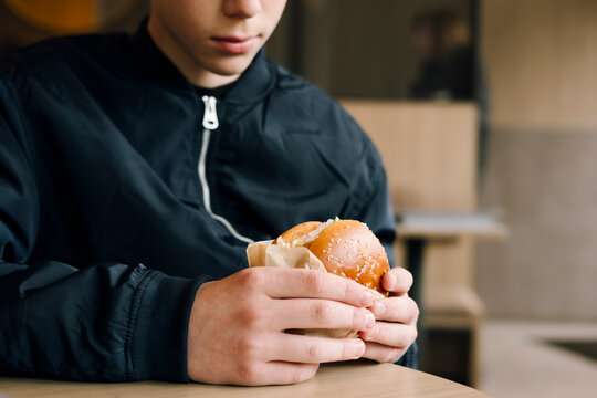 Teenage boy holding hamburger at casual fast food table