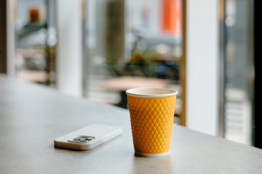 Yellow coffee cup on table with smartphone in cafe