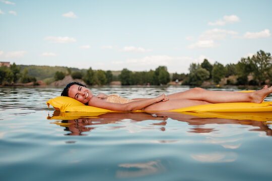 Relaxed woman floating on lake on yellow mat in summer