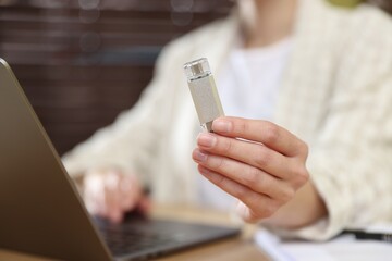 Fototapeta premium Woman with USB flash drive working on laptop at desk, closeup