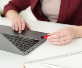 Fototapeta premium Woman with USB flash drive working on laptop at desk, closeup