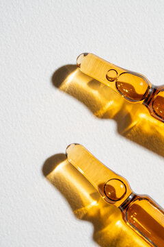 Glass beauty ampule with cosmetic serum on white backdrop