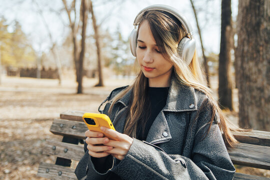 Girl using smartphone with headphones on park bench